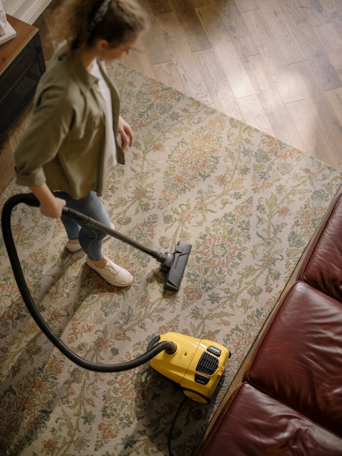 creative-03 Overhead view of a woman vacuuming a carpet at home, highlighting cleanliness and housekeeping.